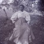 Portrait of older black woman sitting in a chair under a tree, early 20th century